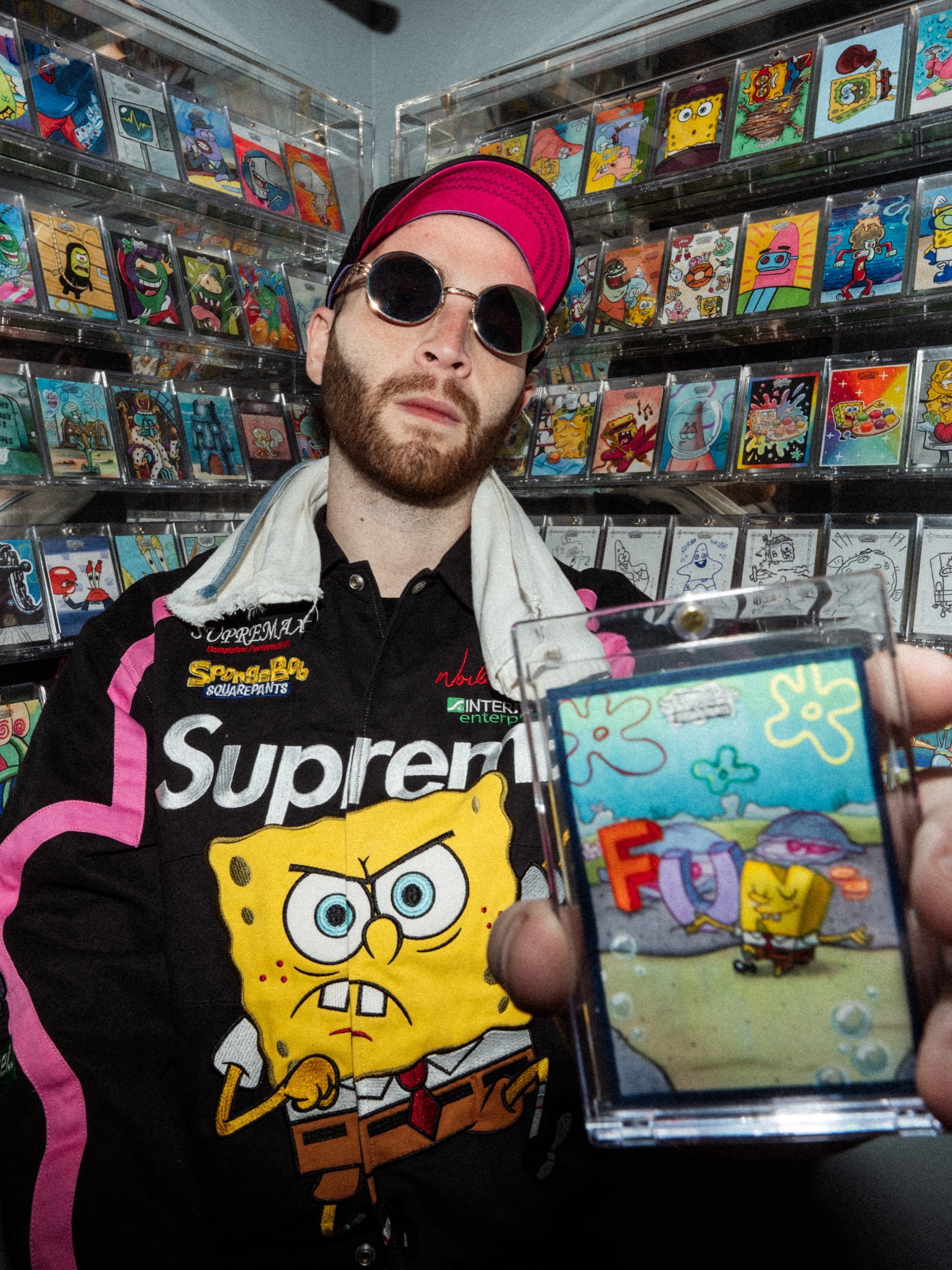 Ari Matlick holding a slabbed SpongeBob trading card up to the camera in front of a wall of displayed cards.