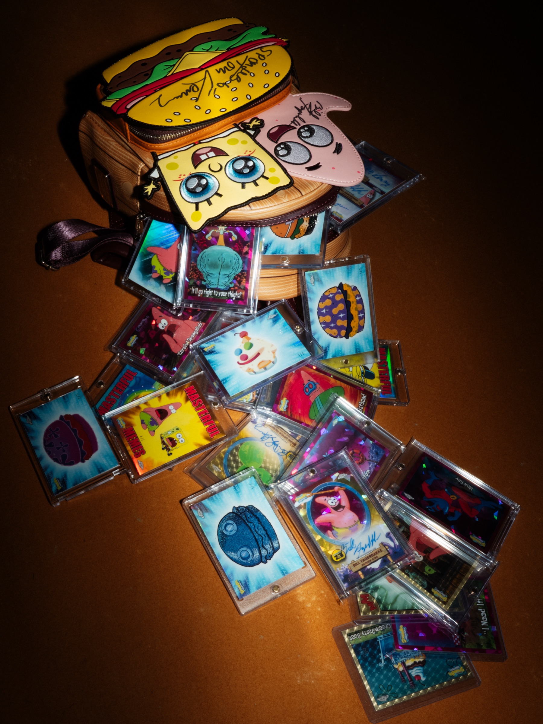 A spread of slabbed SpongeBob trading cards beside a burger-shaped collectible, photographed flat on a warm-lit table.